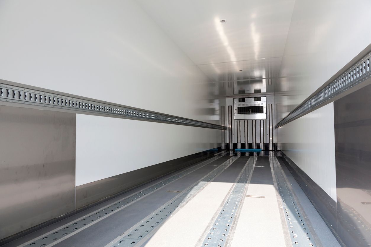 Interior of a refrigerated semi-trailer. White walls, grey floor and metal tracks. Cooling unit visible at end.