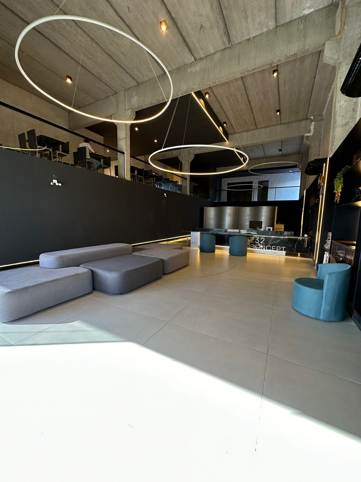 Interior de escritório moderno com paredes cinza e pretas, luminárias circulares e assentos azuis.