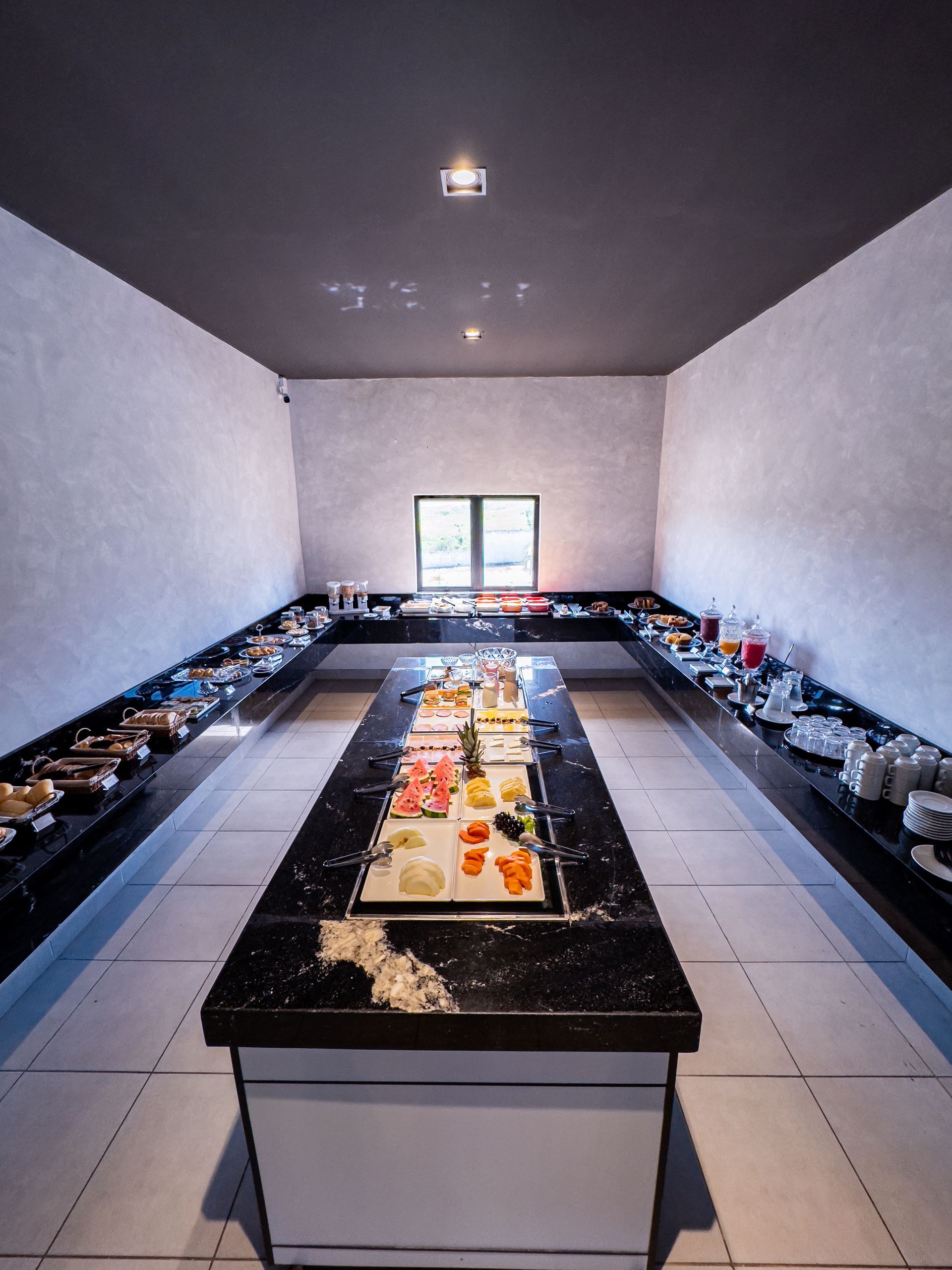 Buffet com longos balcões de mármore exibindo diversos itens alimentícios em uma sala de tons neutros.