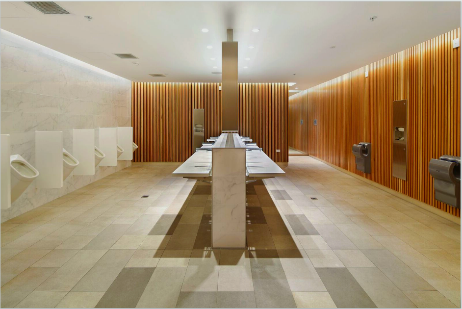Public restroom with urinals, sinks, and wood-paneled walls. Neutral colors, modern design.