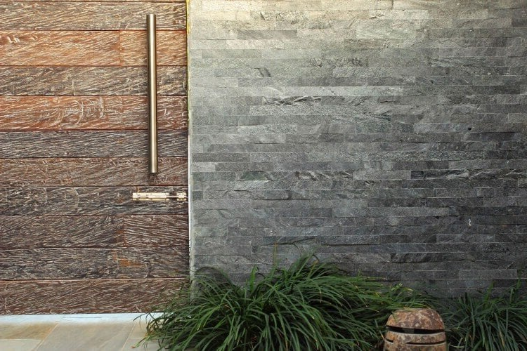 A brick wall with a wooden door and a plant in front of it.
