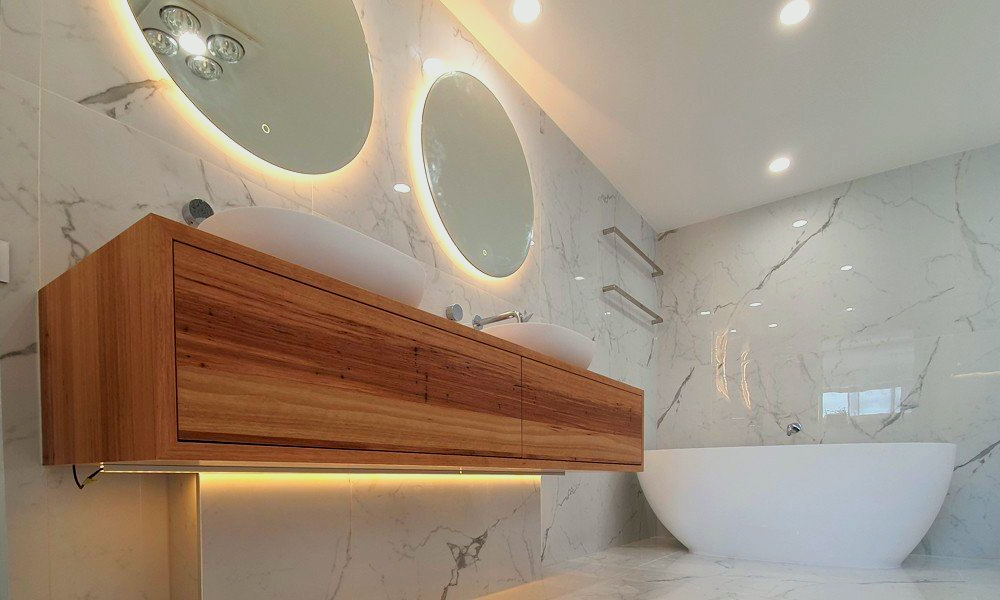 A luxury bathroom with marble walls and flooring, a vanity, two round mirrors and a bathtub.
