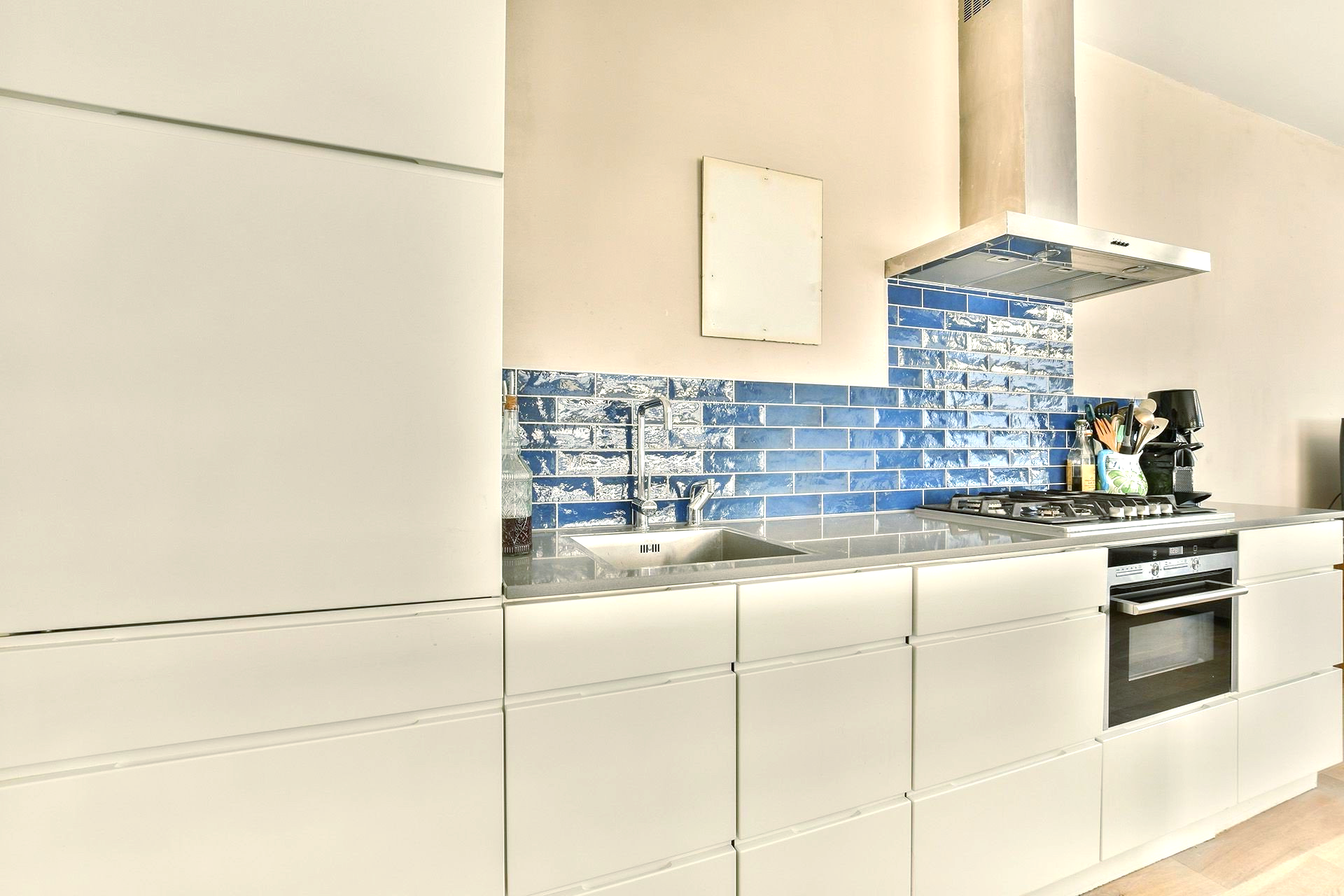 A kitchen with white cabinets and blue tiles.