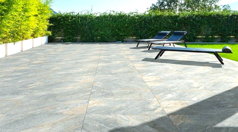 Patio with stone tiles, two lounge chairs, and green hedge backdrop.
