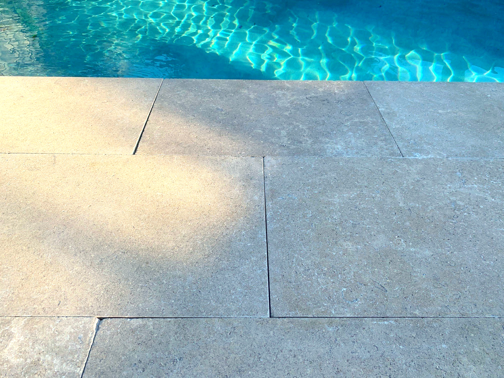Poolside view with blue water and light gray stone tiles.
