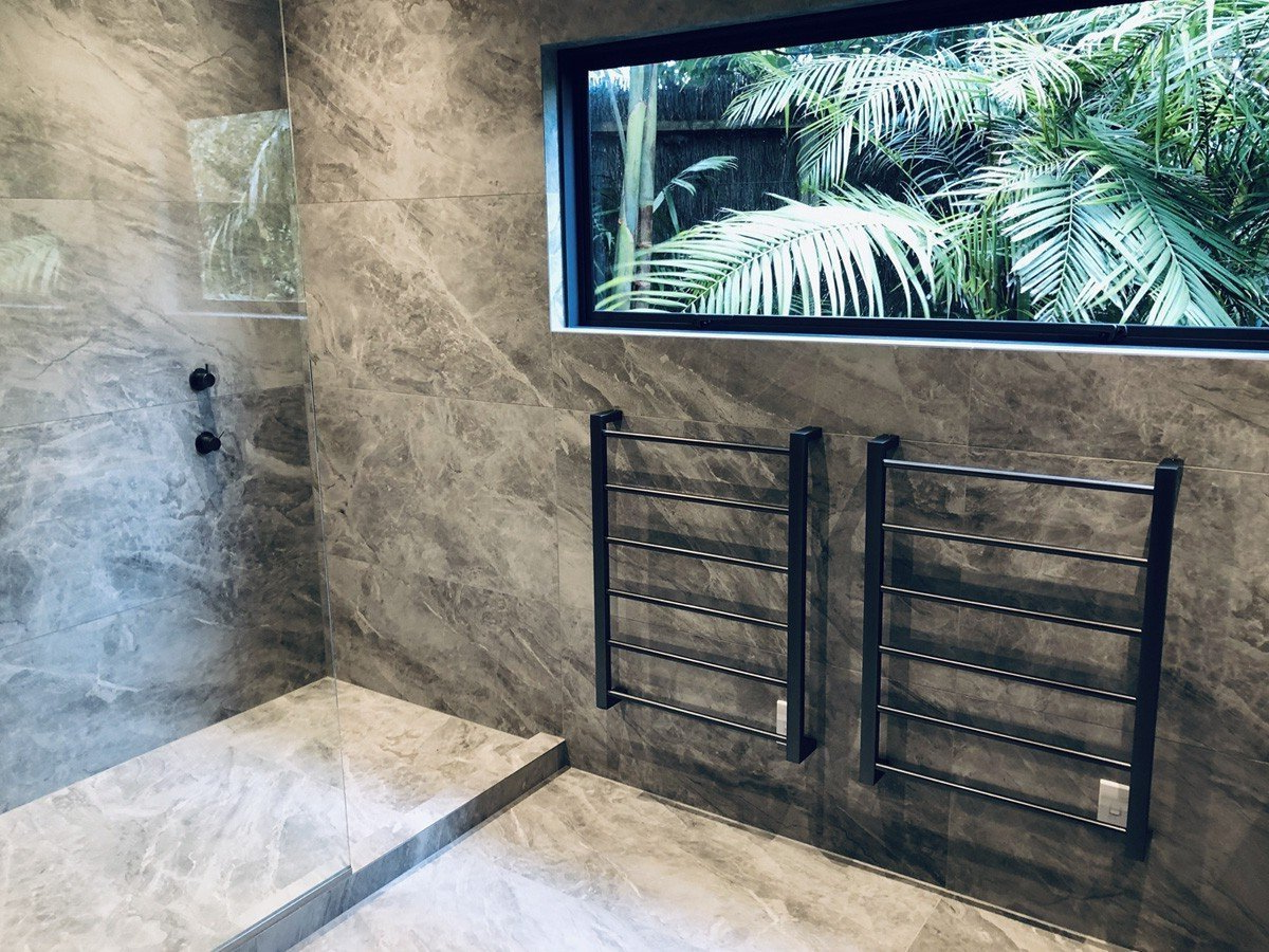 A bathroom with a walk in shower, towel racks and a window.