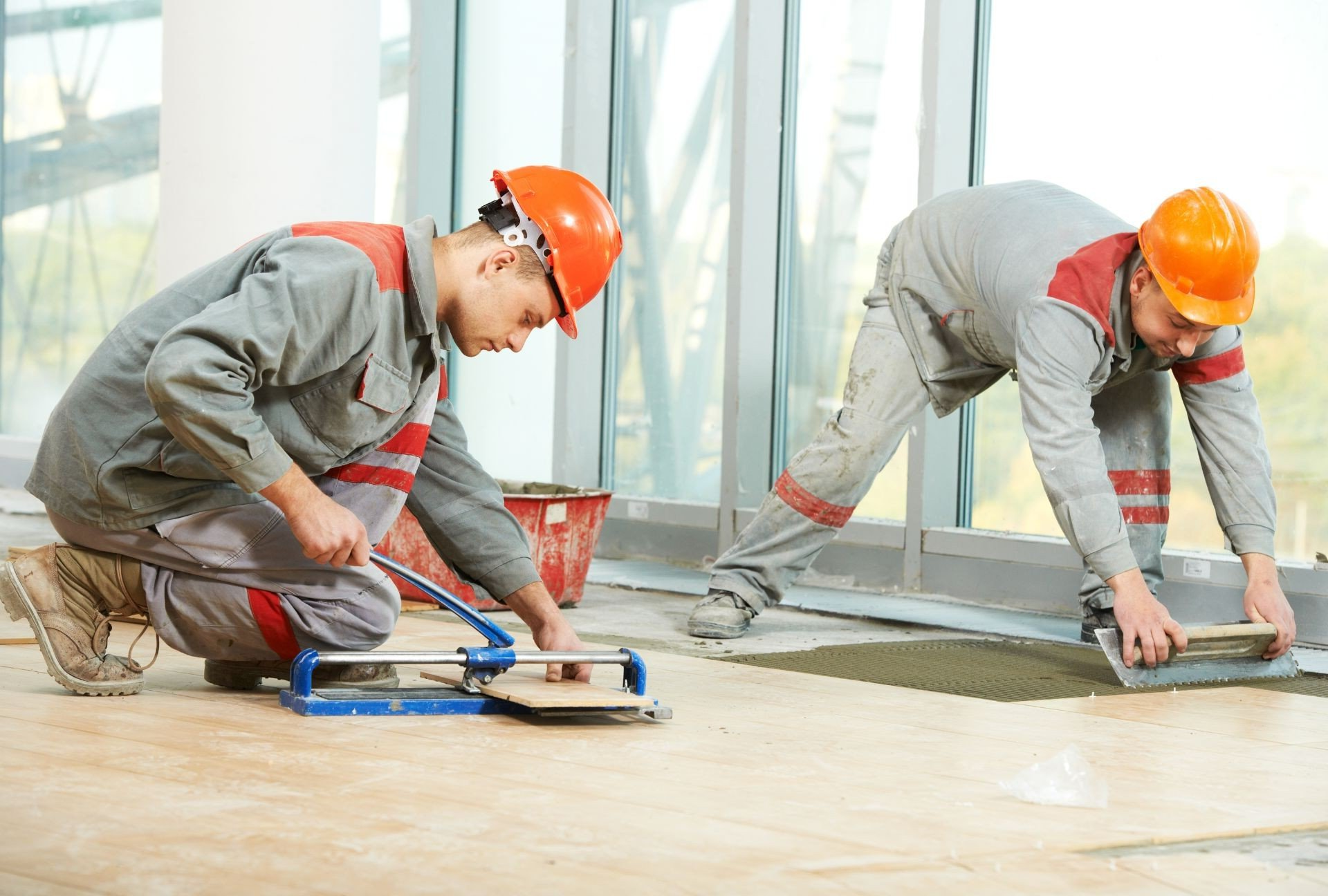 Two construction workers are working on a tile floor.