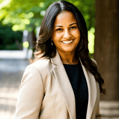 Smiling person in a beige blazer outdoors on a tree-lined path