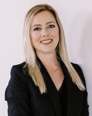 Smiling blonde woman in a black blazer against a light background
