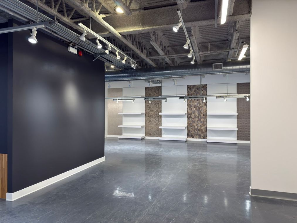 Int&eacute;rieur commercial vide avec murs peints en noir et blanc, pr&eacute;sentoirs de carrelage et plafond industriel.