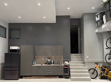 Un int&eacute;rieur moderne avec cuisine grise, escaliers blancs, &eacute;tag&egrave;res, v&eacute;los et &eacute;clairage encastr&eacute;.
