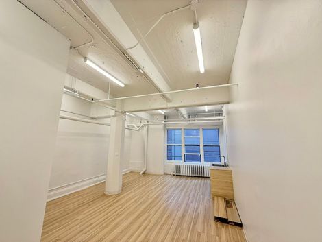 Pi&egrave;ce vide avec murs blancs, plancher en bois et colonne centrale, &eacute;clair&eacute;e par fen&ecirc;tres.