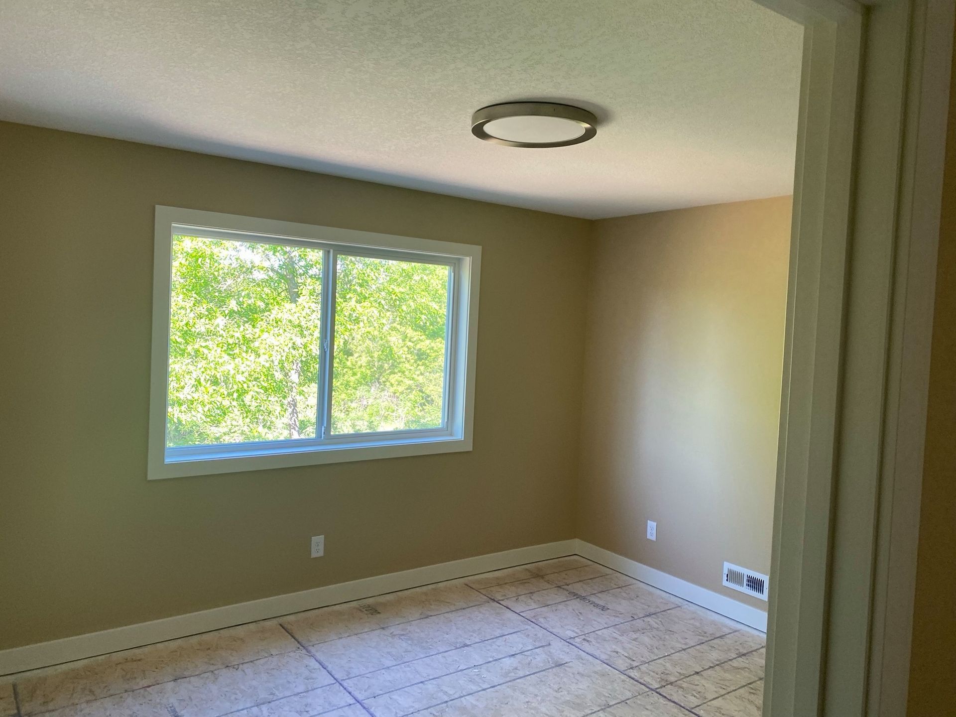 An empty room with a large window and a ceiling light.