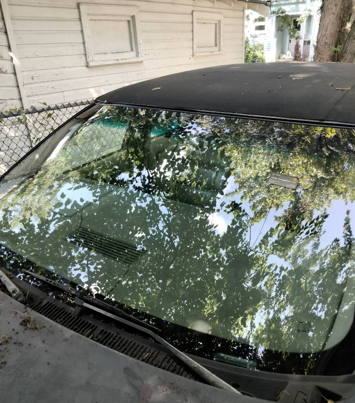 Black convertible car with windshield reflecting trees.