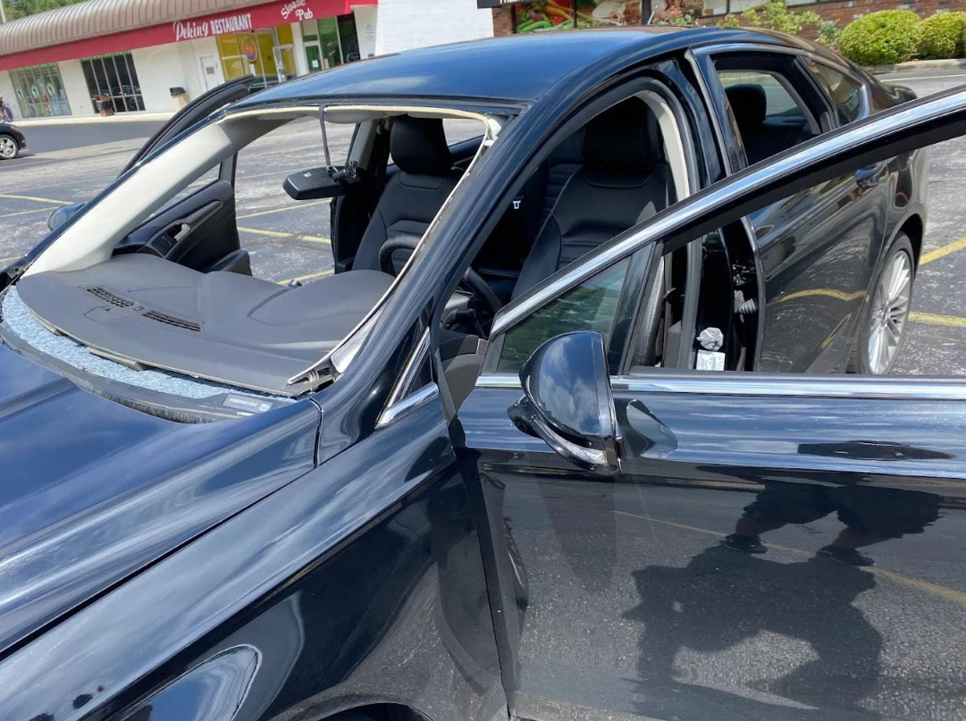 Black car with open doors, missing windshield, parked in a lot.