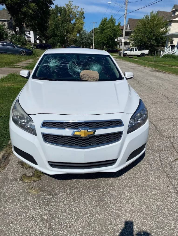 White Chevrolet Malibu with shattered windshield parked on a residential street.