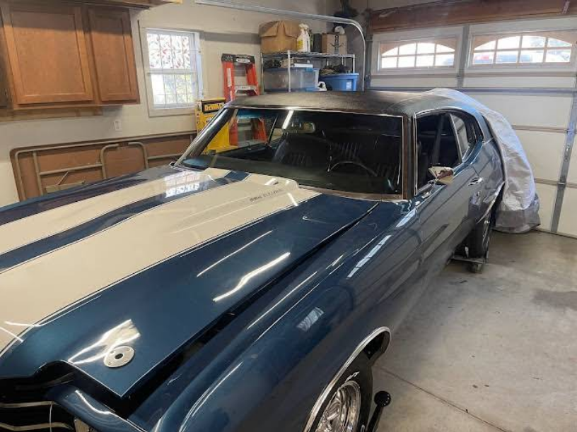Blue classic car with white racing stripes in a garage.