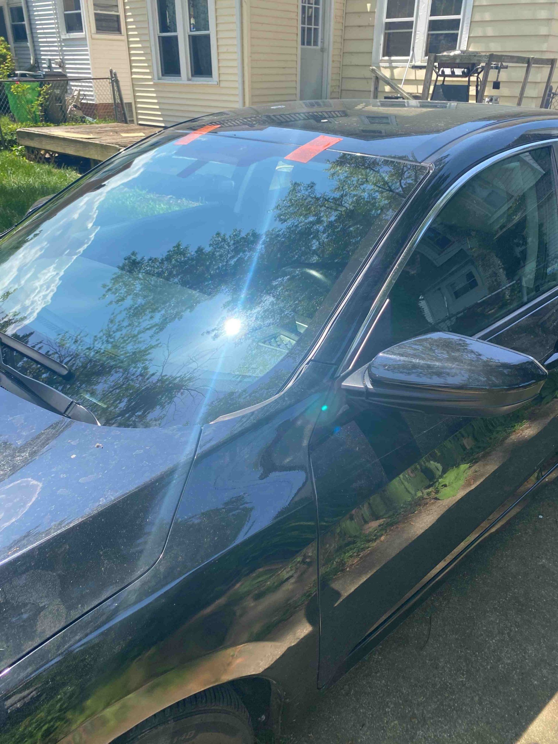 Black car parked outside in sunny weather; orange tape marks on the windshield.