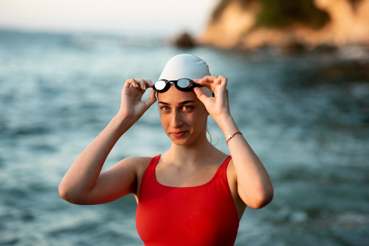 Swimmer in a red suit adjusting goggles at the ocean shore at sunset