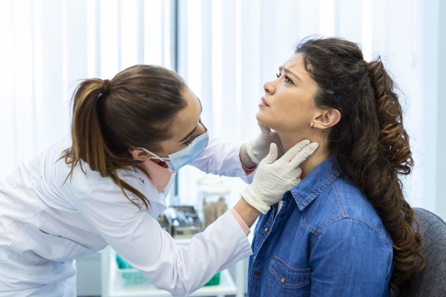 Doctor examining a patient’s throat in a clinic, wearing gloves and a mask