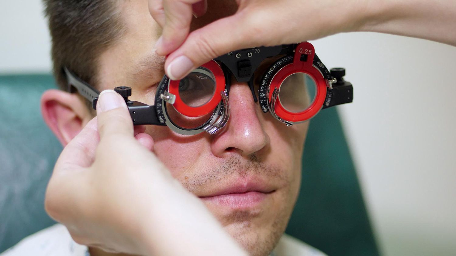 Person wearing red trial lenses while an eye exam is performed