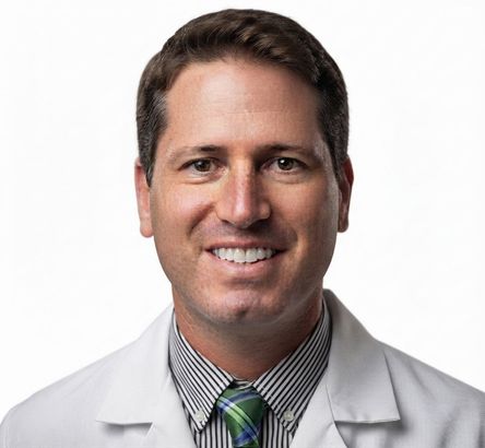 Smiling doctor in white coat with striped shirt and green tie on a plain white background