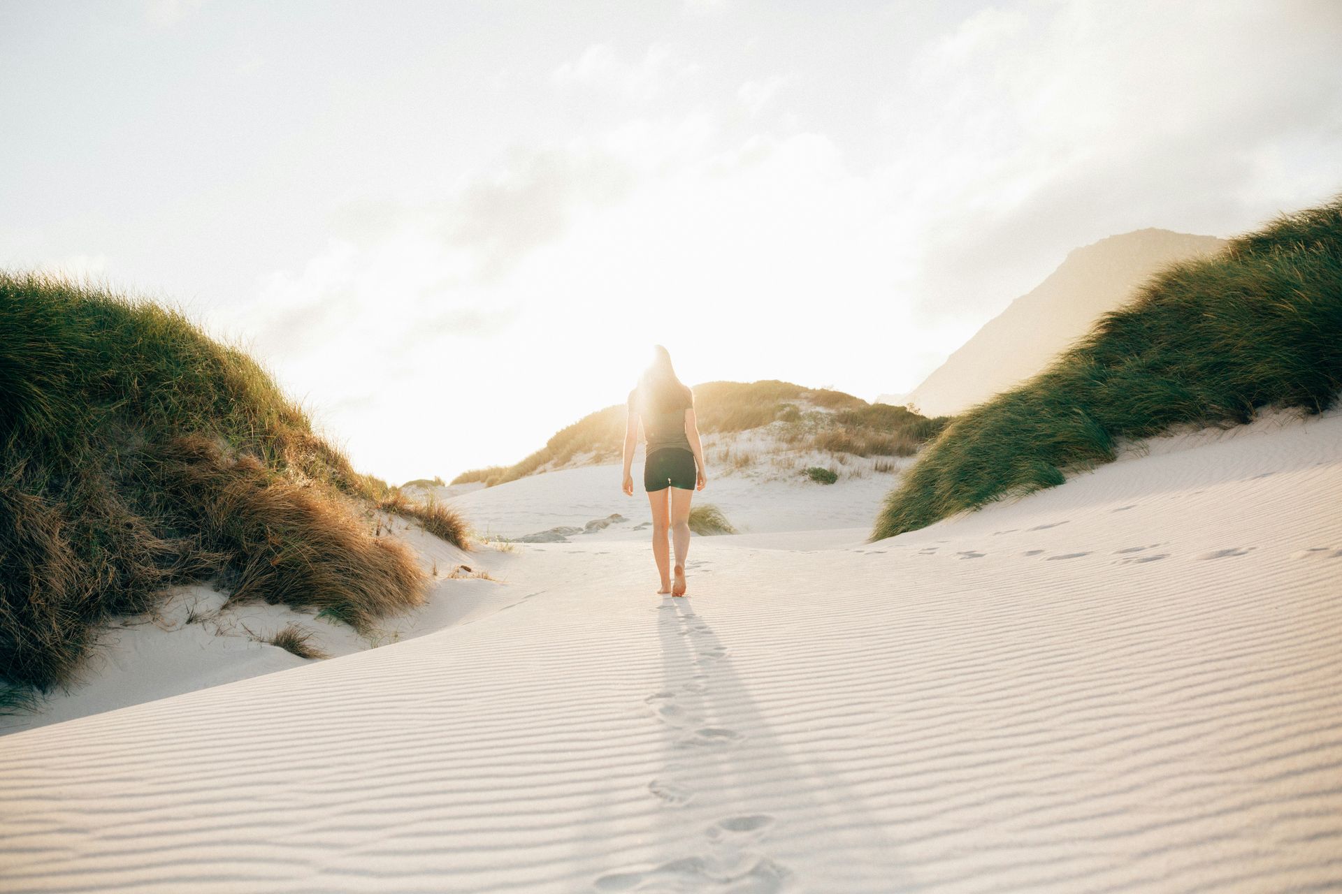Person walking through sunlit sand dunes with grassy mounds trauma recovery