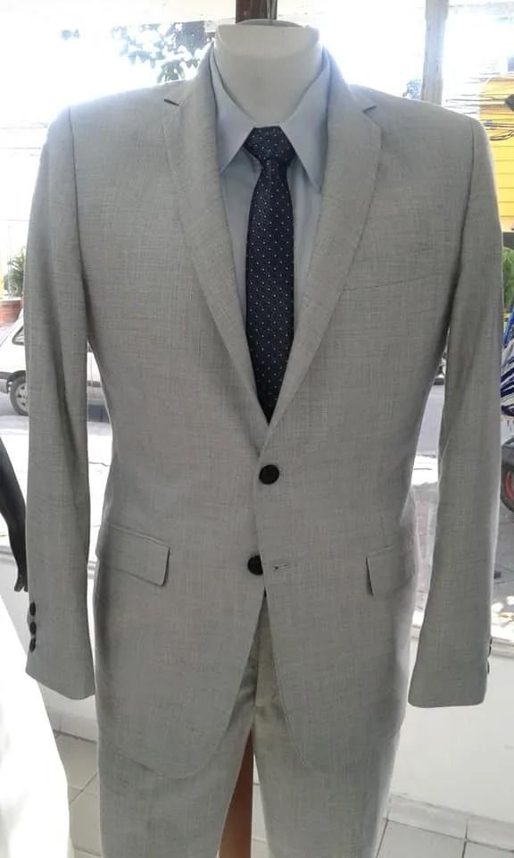 Chaqueta de traje gris claro con corbata oscura estampada en un maniquí sobre un fondo brillante.