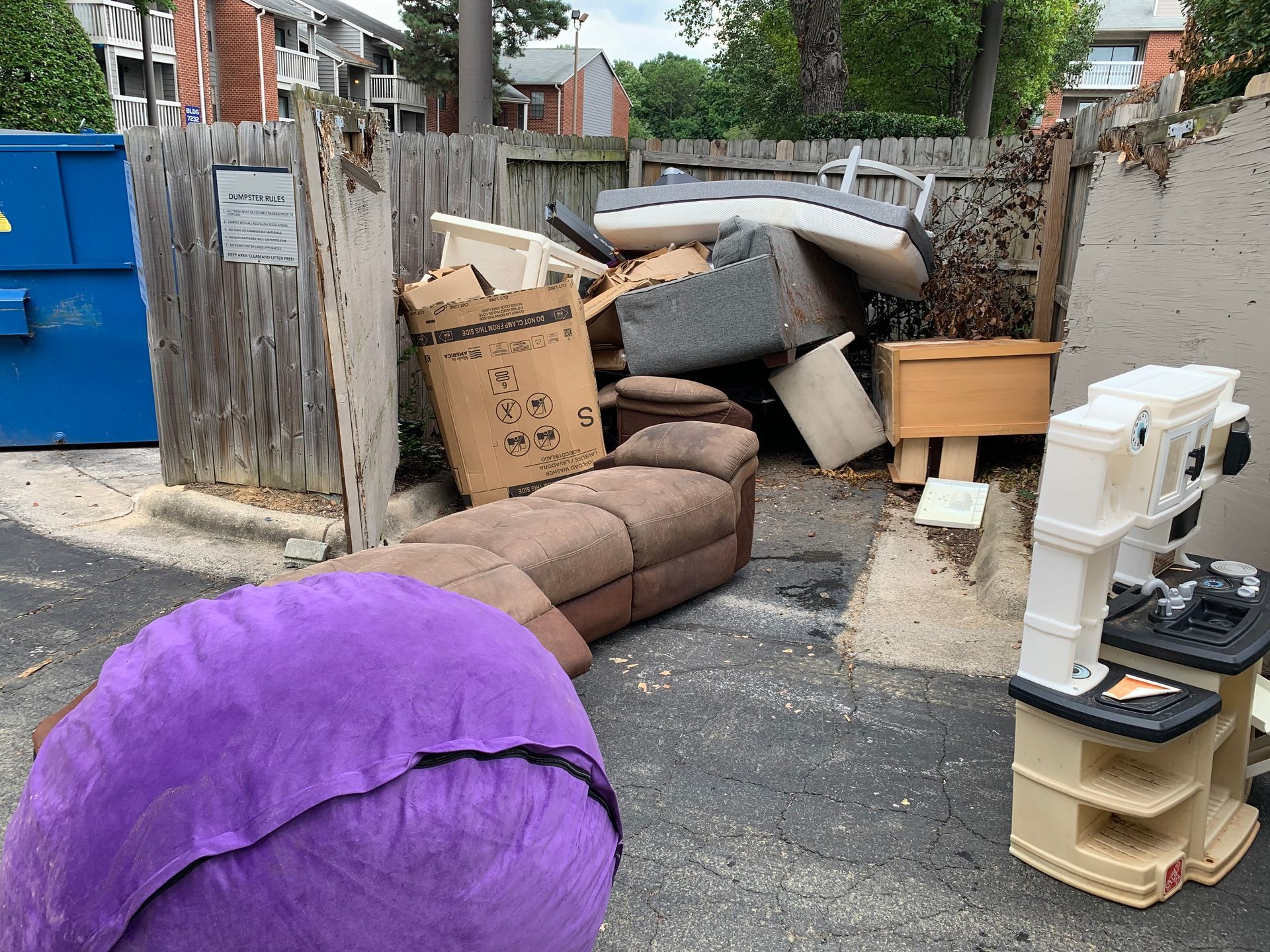 A pile of junk is sitting in a driveway next to a dumpster.