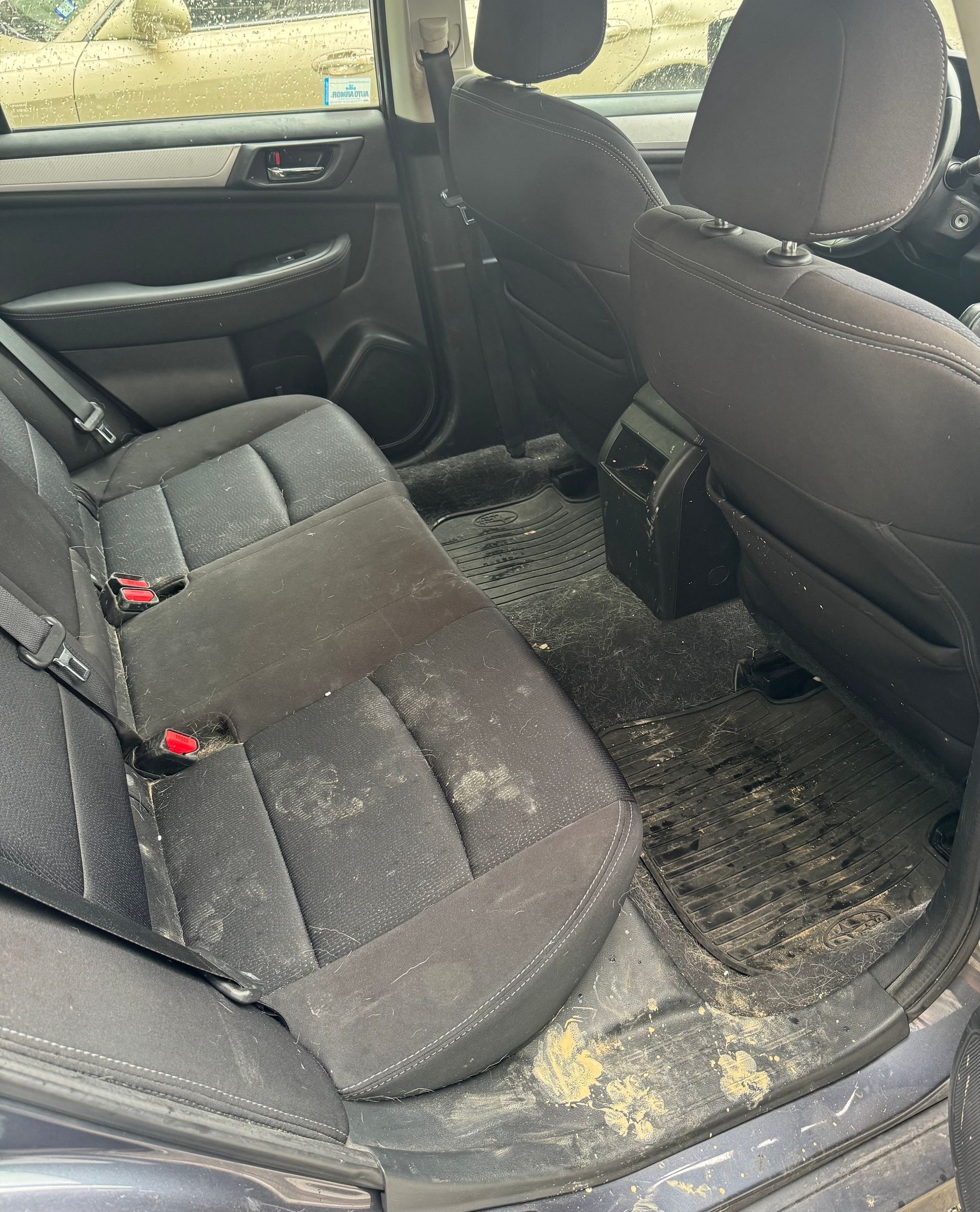 The back seat of a dirty car with a dirty floor.