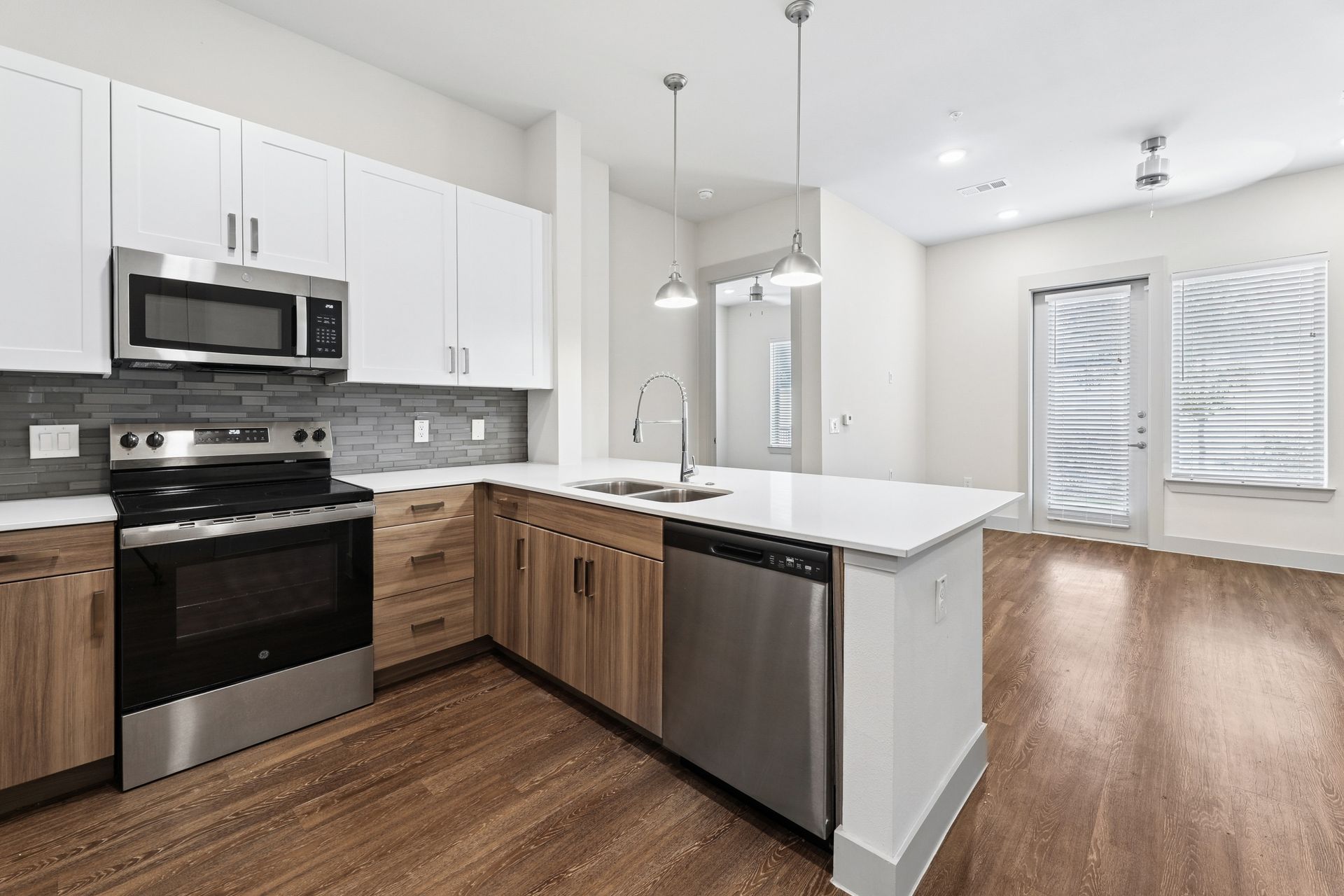 Bright modern kitchen with white cabinets, stainless appliances, and wood flooring opening to a living area