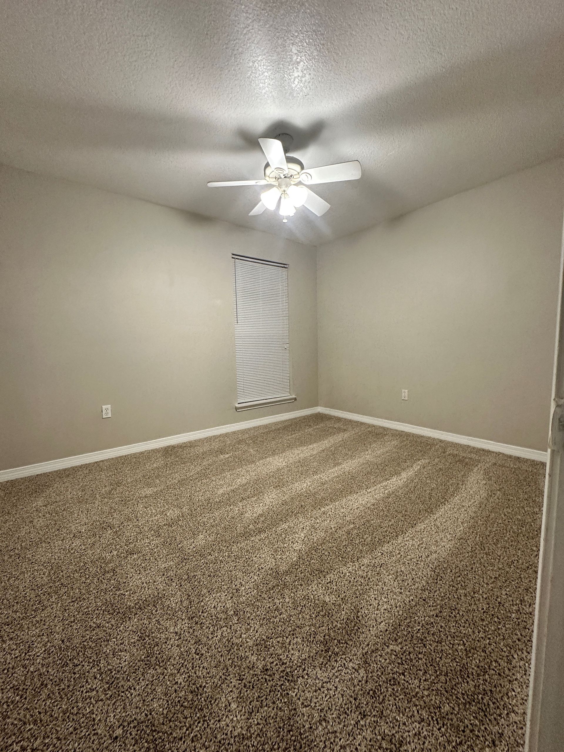 An empty bedroom with a ceiling fan and a window.