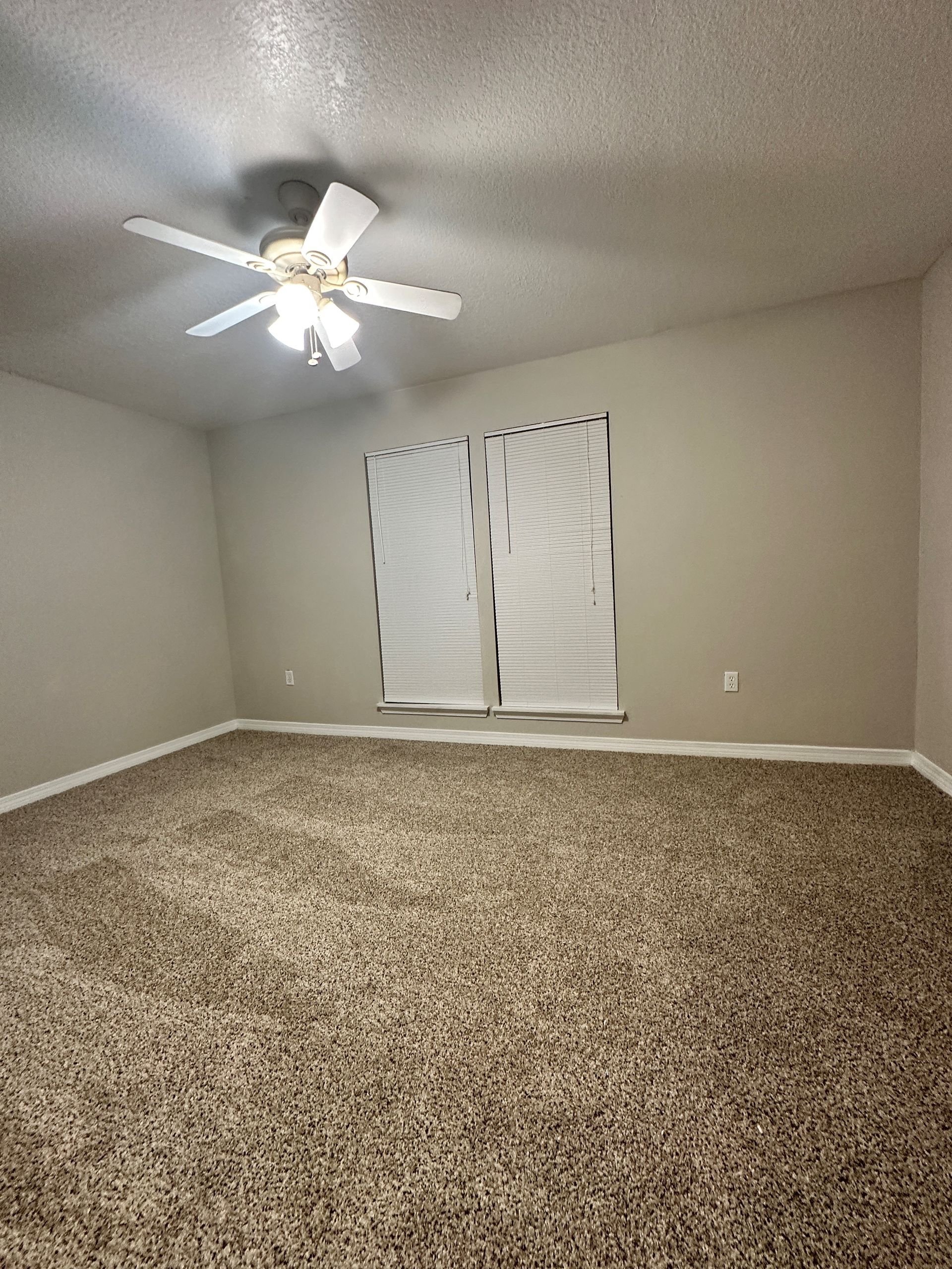 An empty bedroom with a ceiling fan and two windows.