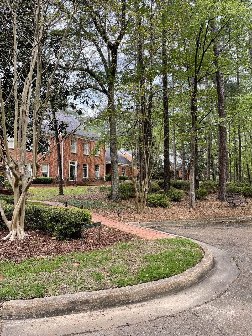 A brick house is surrounded by trees and bushes in a residential area.