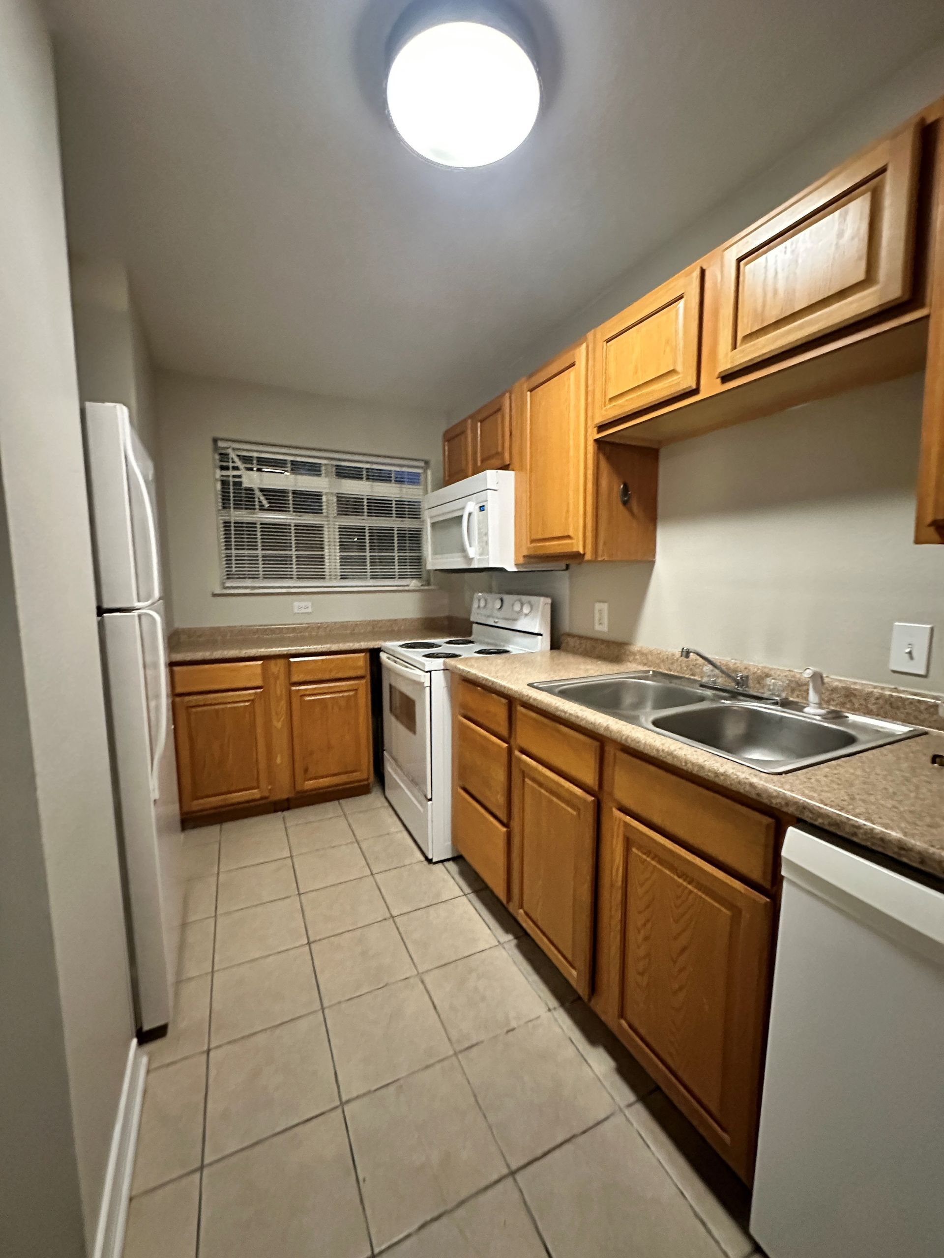 A kitchen with wooden cabinets , a stove , a refrigerator and a sink