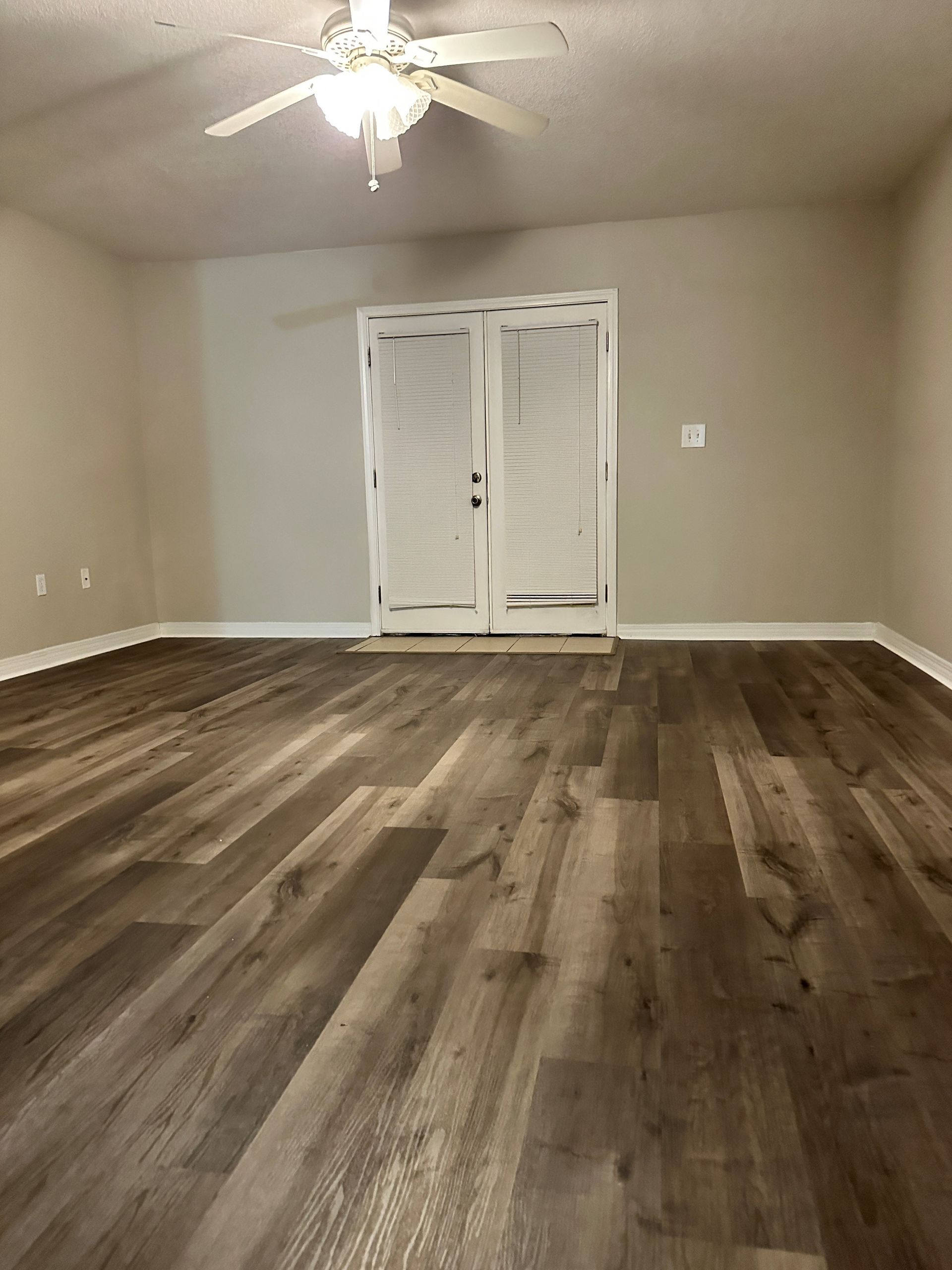 An empty living room with hardwood floors and a ceiling fan.