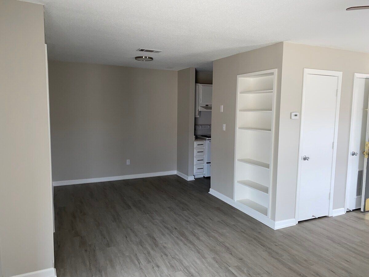 An empty living room with hardwood floors and shelves.