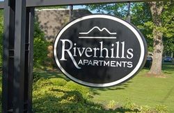 A sign for riverhills apartments is hanging from a pole in the grass.
