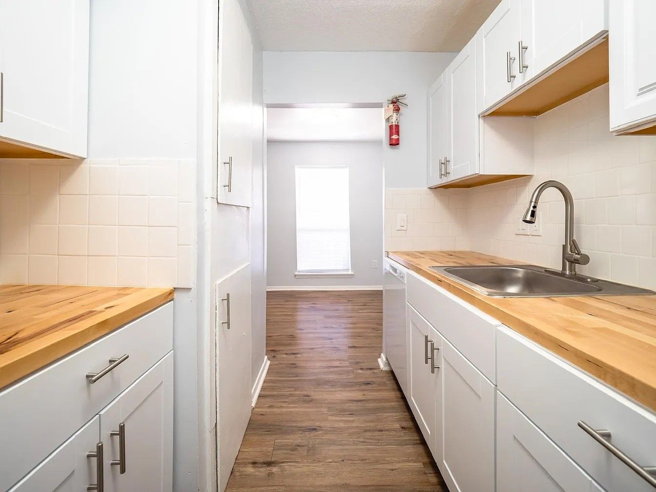A long kitchen with white cabinets and wooden counter tops