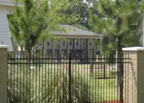 A metal fence surrounds a lush green yard in front of a house.