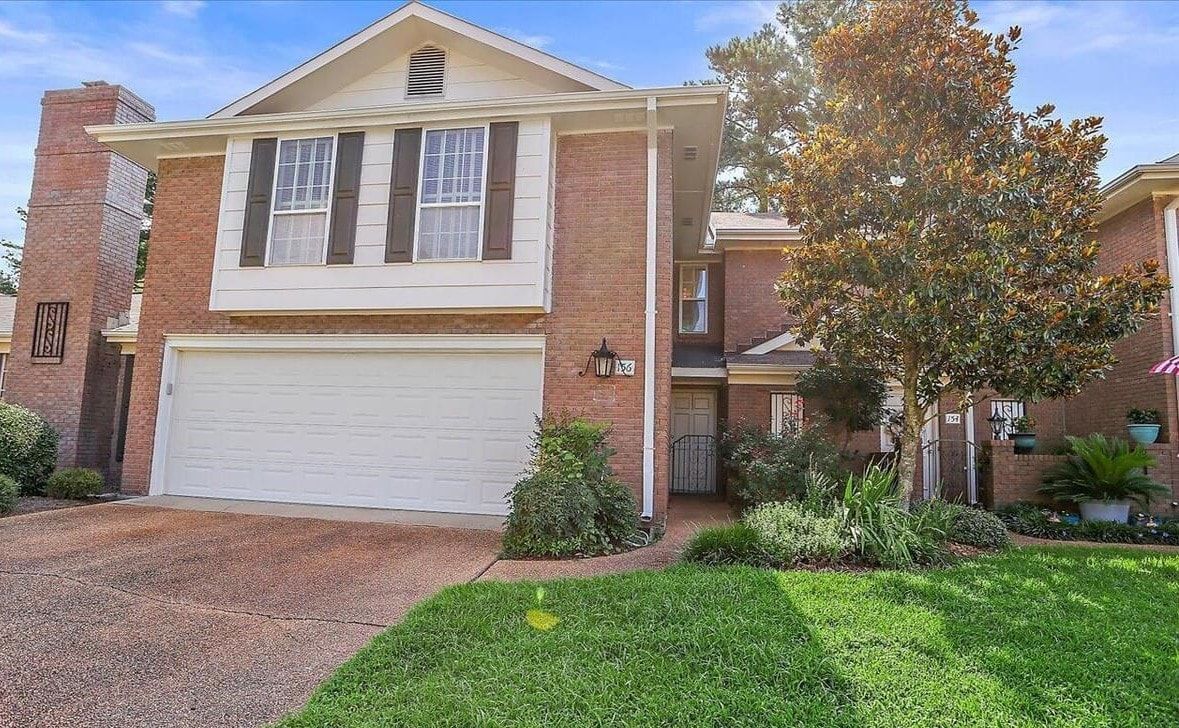 A large brick house with a white garage door and a tree in front of it.