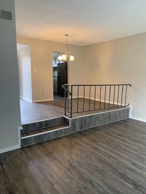 An empty living room with hardwood floors and stairs leading to the kitchen.