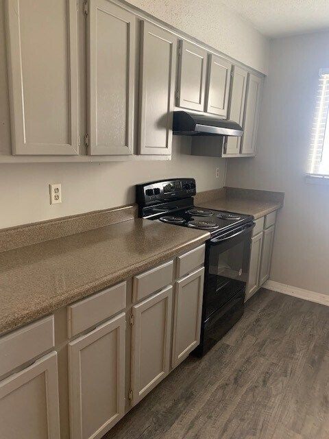 A kitchen with white cabinets , a black stove , and a window.
