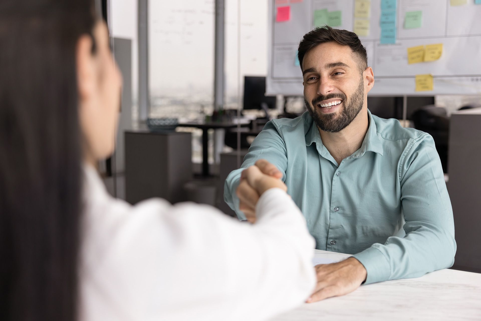 Man in blue shirt smiling, shaking hands with someone out of frame, in an office setting.