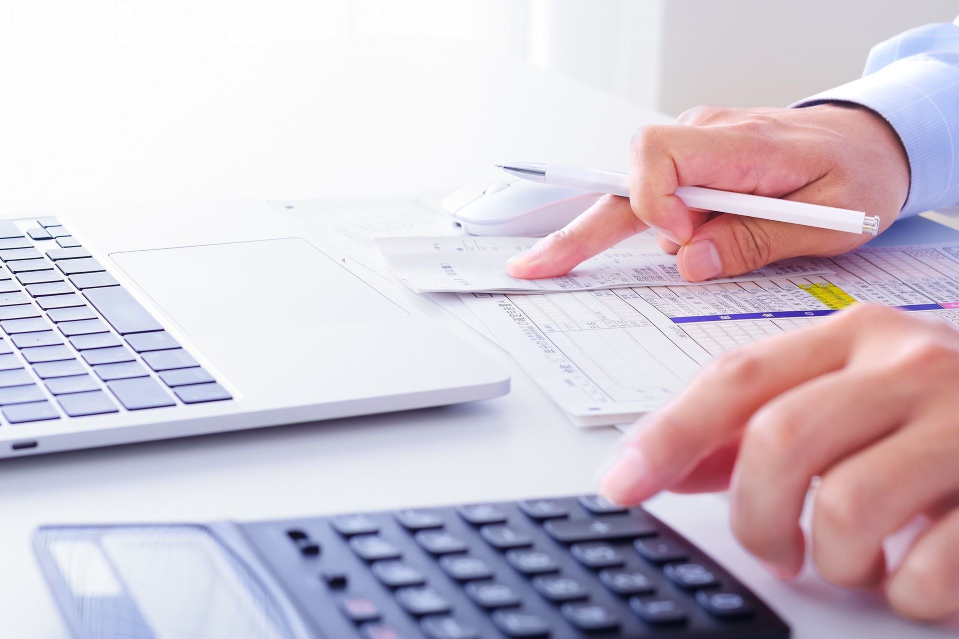 Person using calculator, laptop, and pen to review financial documents at a desk.