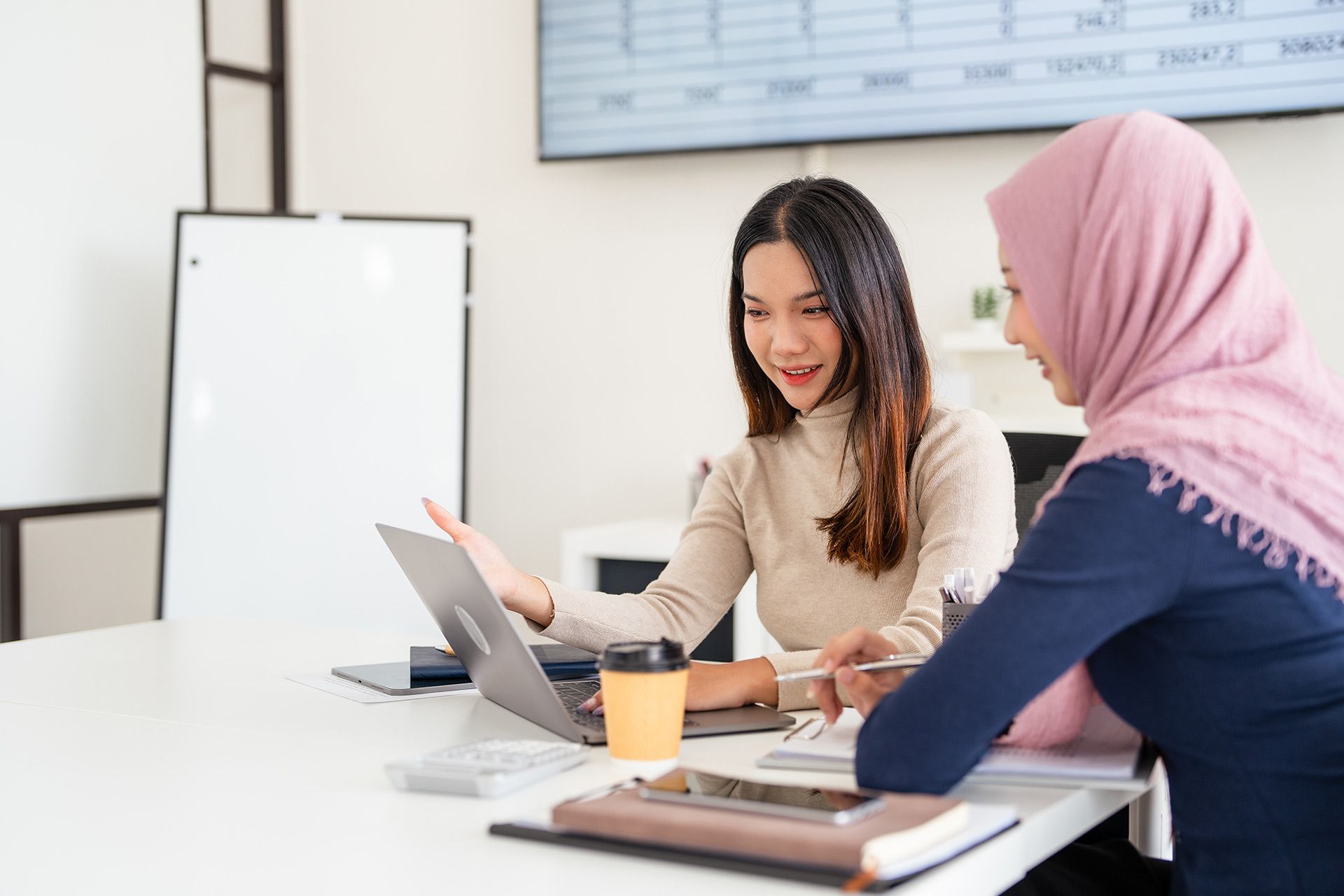 Two women at a desk, looking at a laptop.