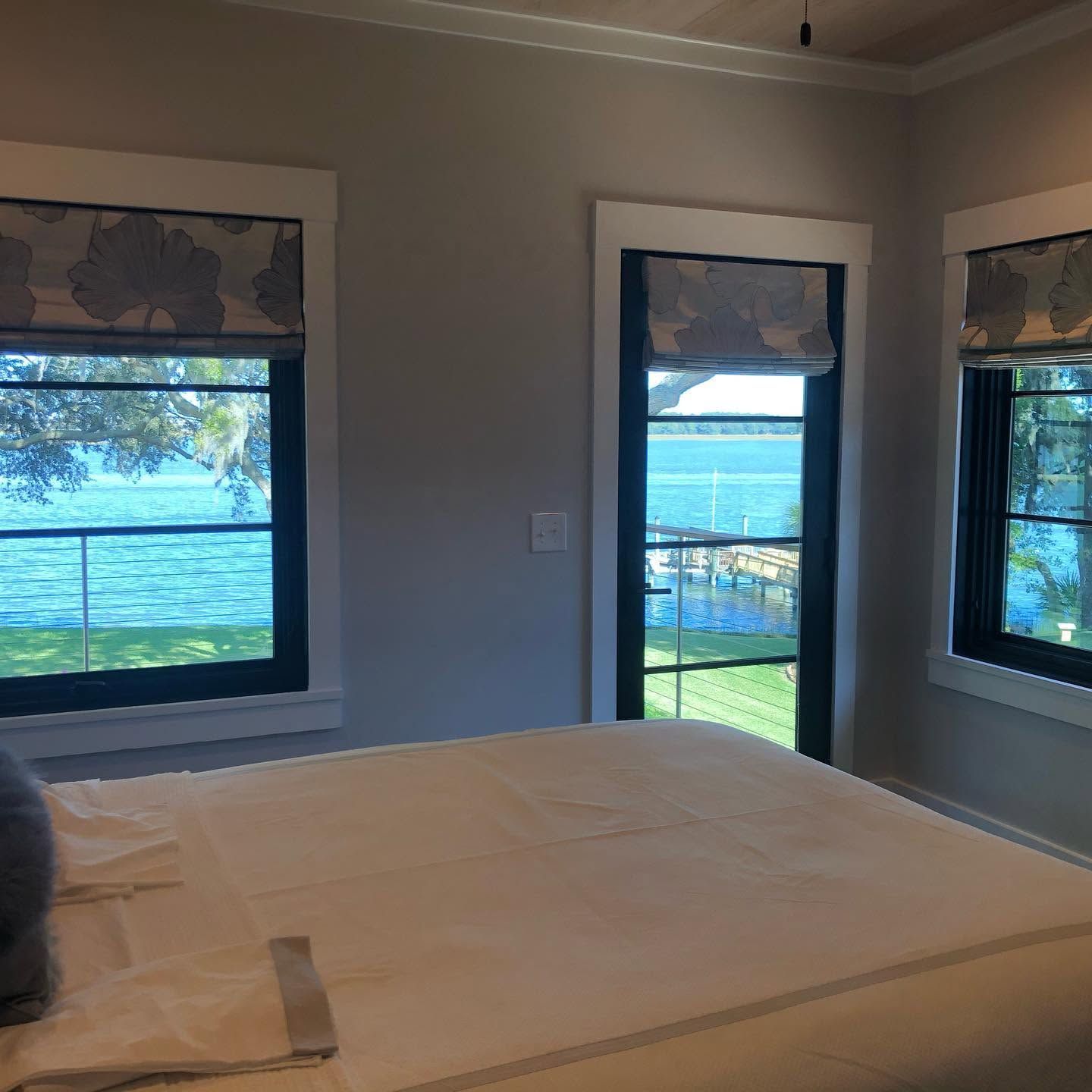 Bedroom with a bed and three windows overlooking a lake or river.