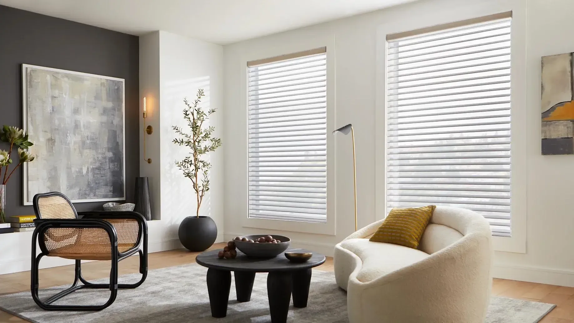 Modern living room with two large windows, beige chair, black coffee table, and abstract wall art.