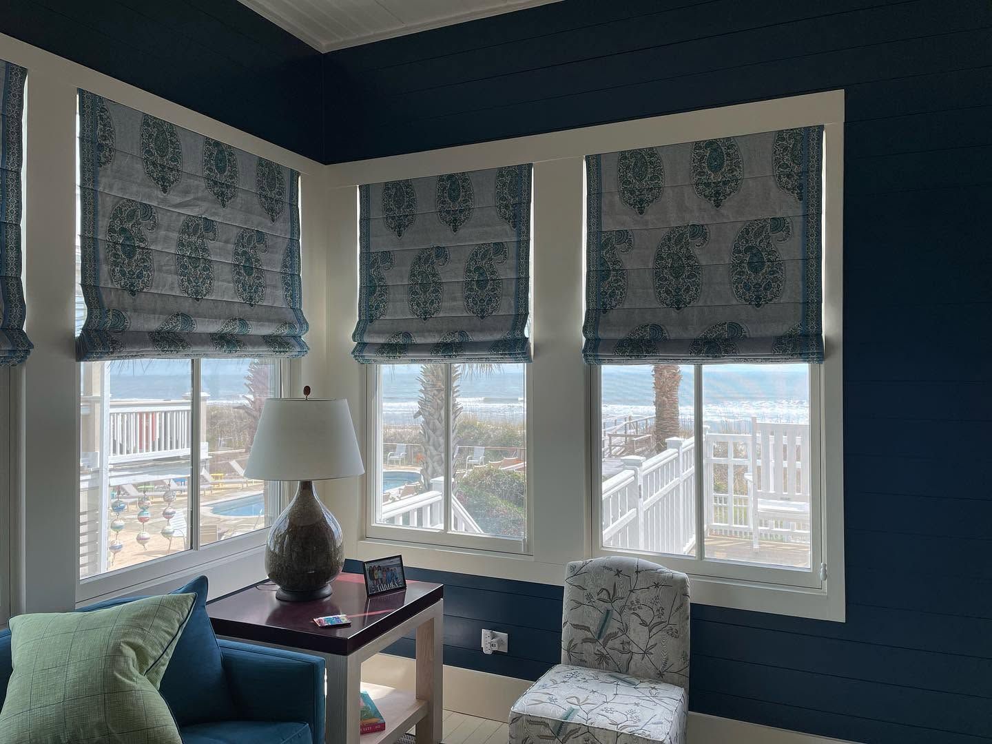 Cozy corner with bay windows, patterned shades, a lamp, and a chair overlooking a snowy city view