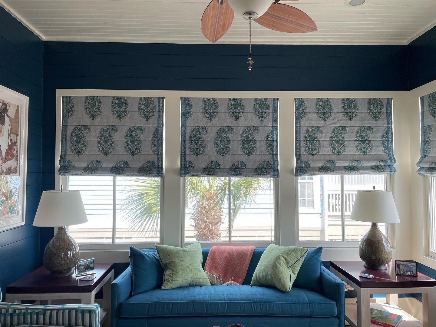 Blue sofa in a bright living room with patterned blinds, lamps, and teal walls